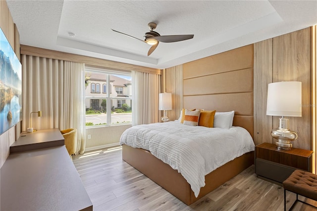 bedroom with light wood-type flooring, a raised ceiling, ceiling fan, and a textured ceiling