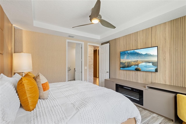 bedroom featuring a tray ceiling, ceiling fan, light hardwood / wood-style floors, and ensuite bath