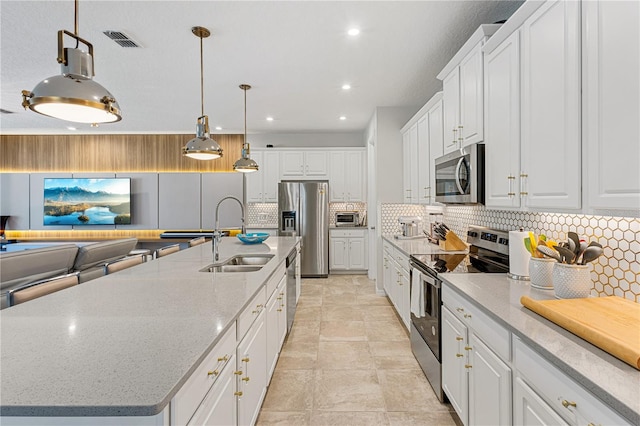 kitchen featuring stainless steel appliances, decorative backsplash, white cabinetry, sink, and a kitchen island with sink