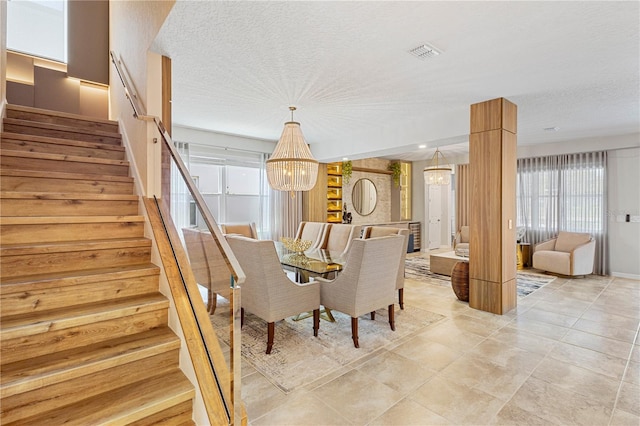 tiled dining space featuring a textured ceiling, an inviting chandelier, and decorative columns