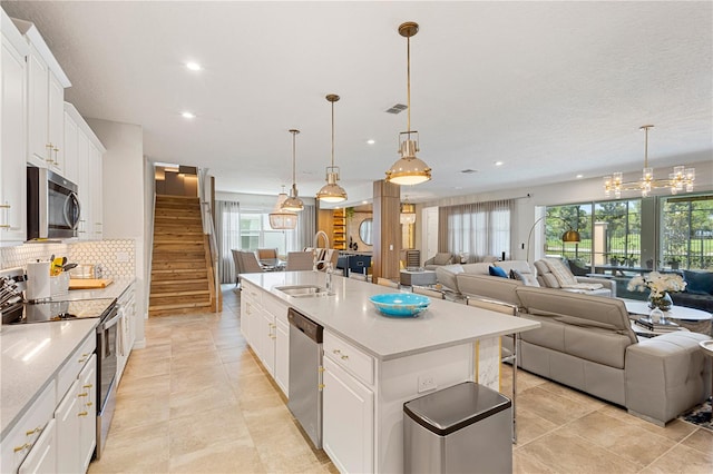 kitchen with stainless steel appliances, sink, a kitchen island with sink, white cabinets, and light tile patterned floors