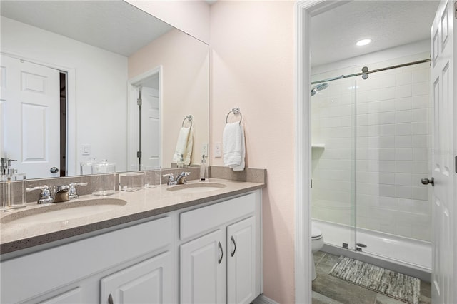 bathroom with dual bowl vanity, a textured ceiling, tile patterned flooring, toilet, and a shower with door