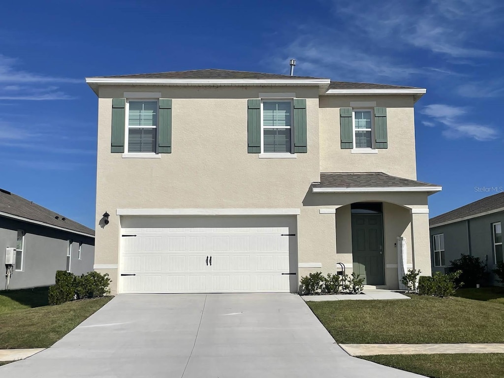 traditional-style home with an attached garage, a front yard, concrete driveway, and stucco siding