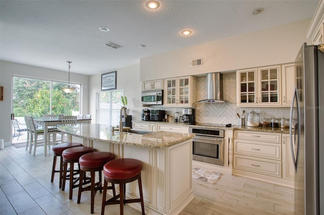 kitchen featuring decorative backsplash, wall chimney exhaust hood, a kitchen island with sink, appliances with stainless steel finishes, and sink