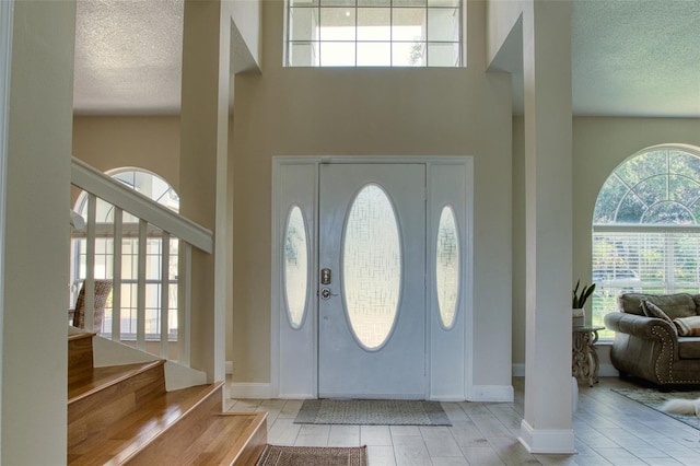 foyer featuring light hardwood / wood-style floors, a towering ceiling, and a textured ceiling