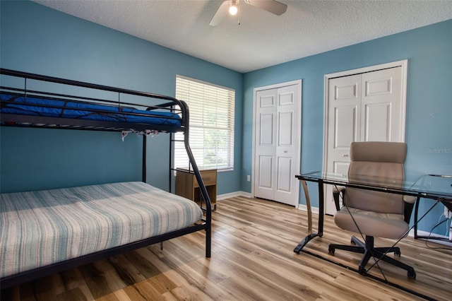 bedroom featuring ceiling fan, a textured ceiling, light hardwood / wood-style flooring, and two closets