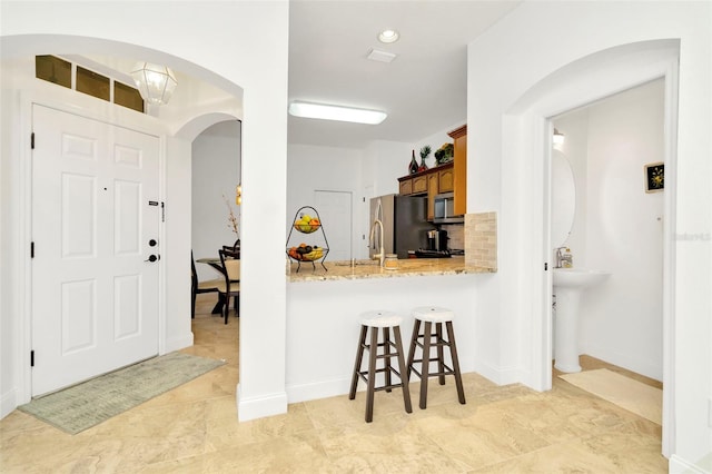 kitchen featuring a kitchen bar, sink, light stone counters, light tile patterned floors, and stainless steel appliances