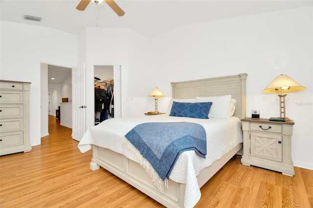 bedroom with light wood-type flooring, vaulted ceiling, ceiling fan, and a walk in closet