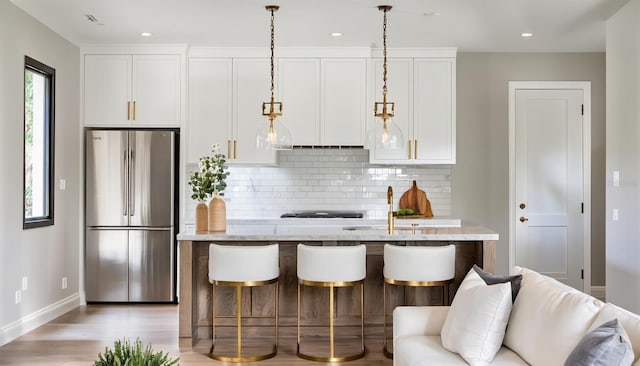 kitchen featuring decorative backsplash, stainless steel refrigerator, light wood-type flooring, pendant lighting, and white cabinets