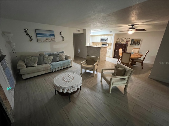 living room featuring a textured ceiling, wood finish floors, visible vents, and a ceiling fan