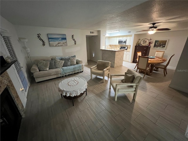 living area featuring wood finish floors, a fireplace, visible vents, a ceiling fan, and a textured ceiling