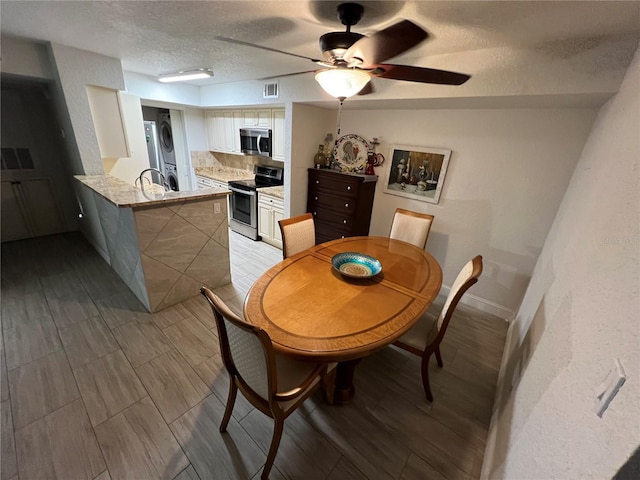 dining room featuring a textured ceiling, visible vents, a ceiling fan, baseboards, and light wood finished floors