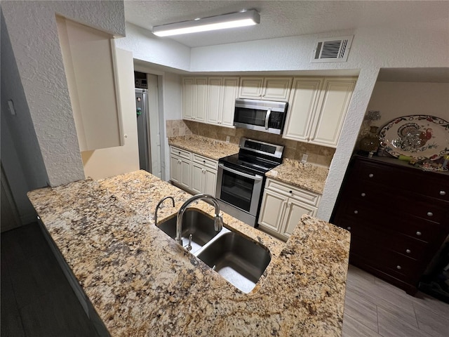 kitchen featuring light stone counters, a sink, visible vents, appliances with stainless steel finishes, and tasteful backsplash