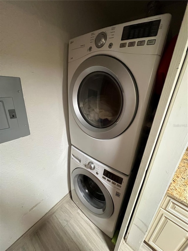 washroom featuring stacked washer / drying machine, laundry area, electric panel, and baseboards