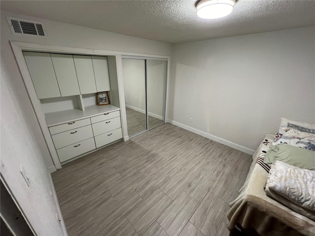 unfurnished bedroom featuring a textured ceiling, visible vents, baseboards, a closet, and light wood-type flooring