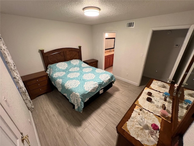 bedroom featuring light wood-type flooring, visible vents, a textured ceiling, and baseboards