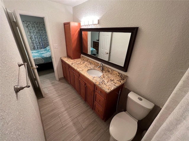 bathroom featuring a textured wall, connected bathroom, vanity, and toilet