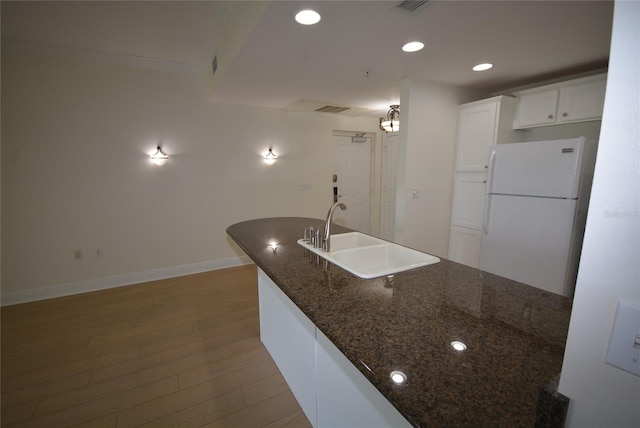 kitchen with sink, light wood-type flooring, white cabinets, dark stone counters, and white refrigerator