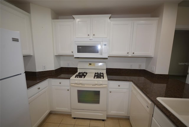 kitchen with light tile patterned floors, dark stone countertops, white appliances, and white cabinets