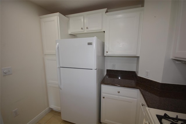 kitchen with dark stone counters, white cabinets, light tile patterned floors, and white refrigerator