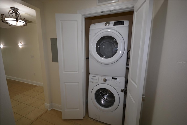 clothes washing area featuring electric panel, light tile patterned floors, and stacked washer / dryer