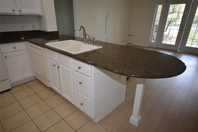 kitchen with light wood-type flooring, white cabinets, dishwasher, sink, and dark stone countertops