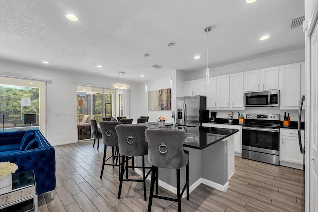 kitchen with hanging light fixtures, white cabinetry, appliances with stainless steel finishes, a breakfast bar area, and a center island with sink