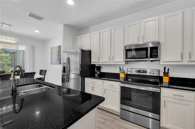 kitchen with dark stone counters, sink, appliances with stainless steel finishes, a textured ceiling, and white cabinets