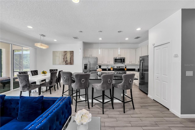 kitchen featuring stainless steel appliances, an island with sink, a textured ceiling, pendant lighting, and white cabinets