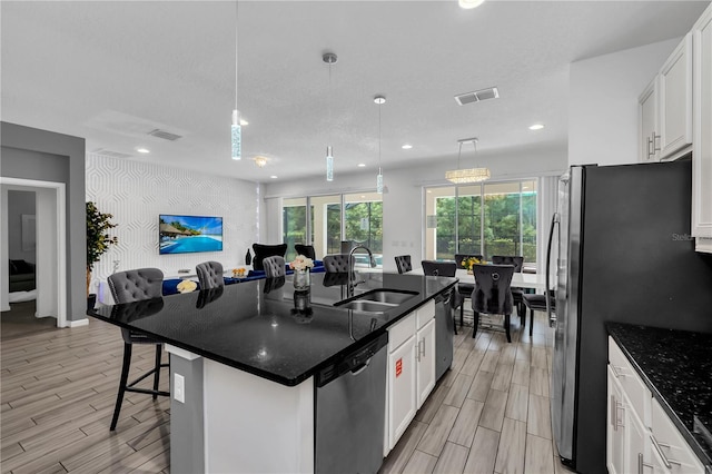 kitchen featuring appliances with stainless steel finishes, light hardwood / wood-style floors, a kitchen island with sink, white cabinets, and hanging light fixtures