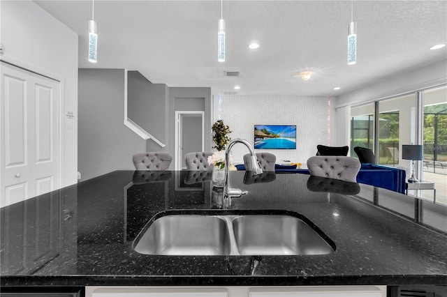 kitchen with sink, dark stone countertops, decorative light fixtures, an island with sink, and a textured ceiling