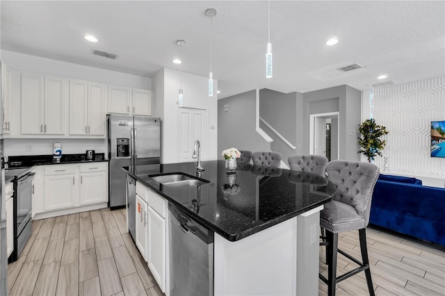 kitchen featuring appliances with stainless steel finishes, white cabinetry, sink, an island with sink, and light wood-type flooring