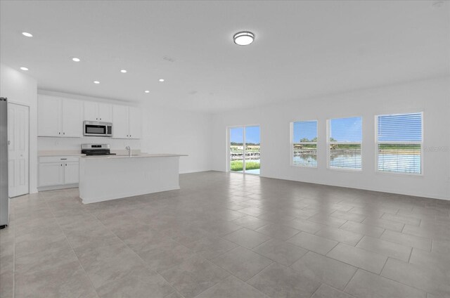 kitchen with white cabinetry, a kitchen island with sink, light tile patterned flooring, range, and sink