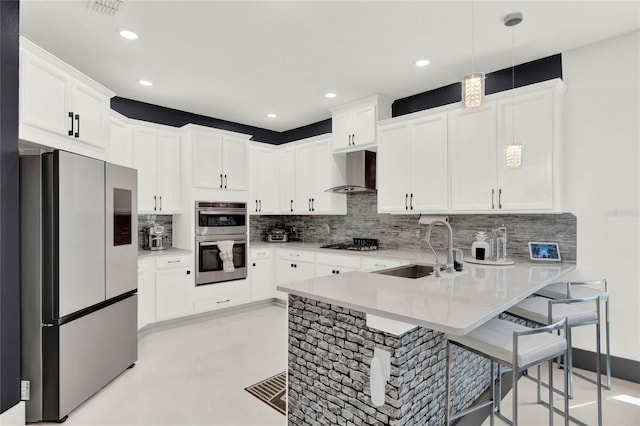 kitchen featuring appliances with stainless steel finishes, sink, decorative backsplash, wall chimney range hood, and kitchen peninsula