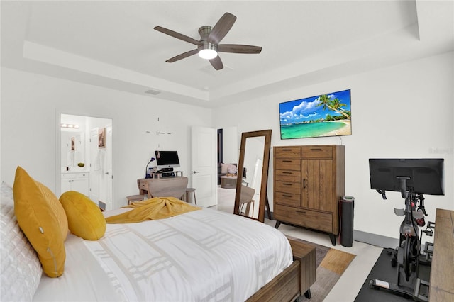 bedroom with connected bathroom, ceiling fan, light hardwood / wood-style flooring, and a tray ceiling