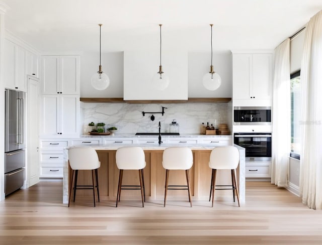 kitchen featuring decorative backsplash, a center island with sink, stainless steel refrigerator, and white cabinetry