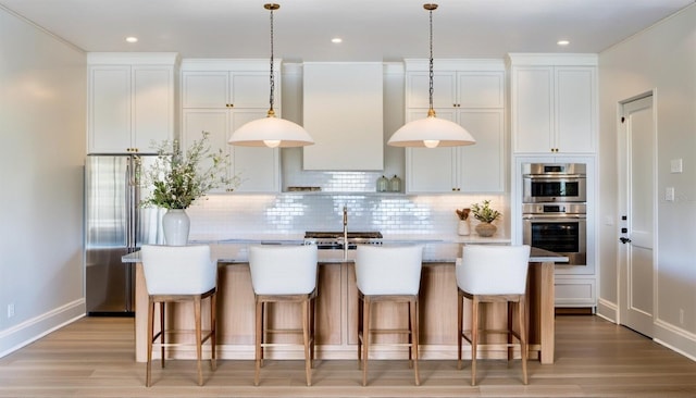 kitchen with a kitchen island with sink, light hardwood / wood-style flooring, decorative backsplash, and white cabinets