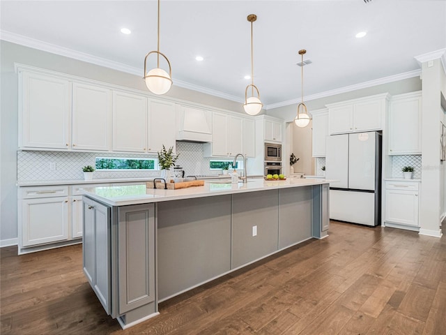 kitchen with appliances with stainless steel finishes, white cabinetry, custom exhaust hood, hanging light fixtures, and a center island with sink