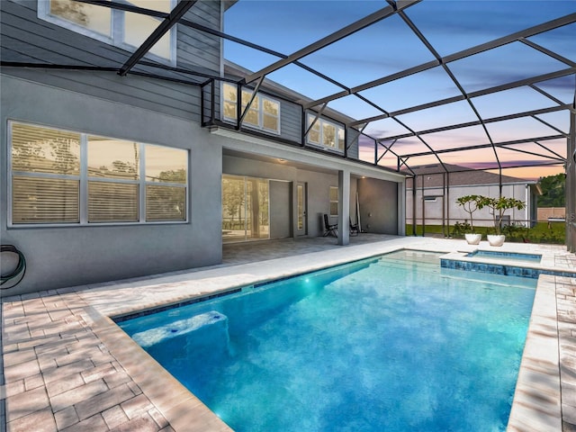 pool at dusk with an in ground hot tub, a lanai, and a patio