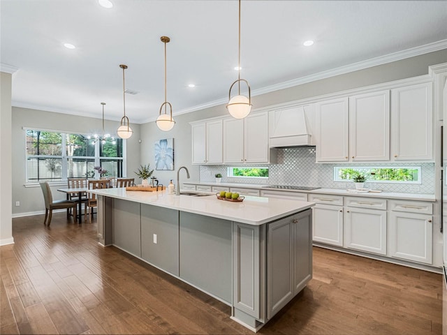 kitchen with sink, white cabinetry, hanging light fixtures, custom range hood, and a kitchen island with sink