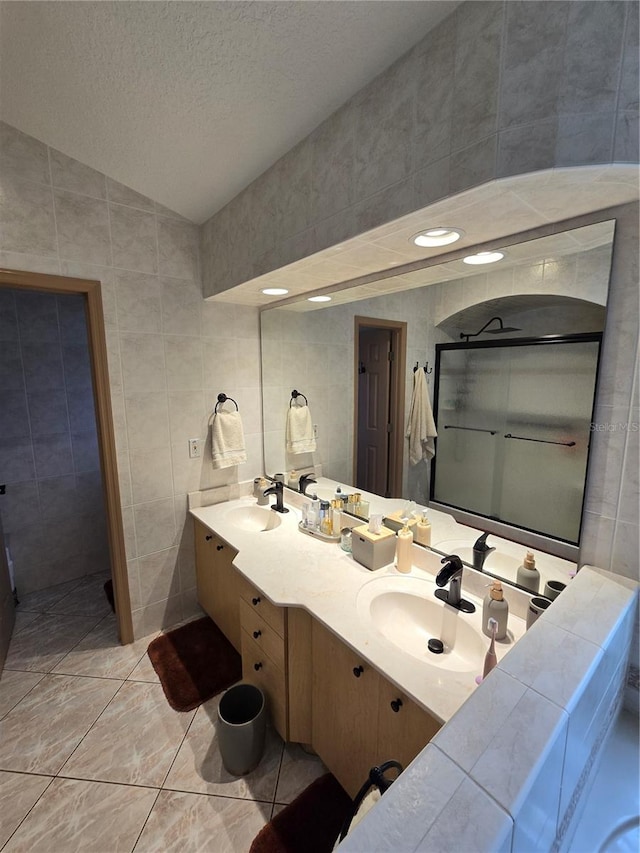 bathroom featuring a textured ceiling, tile walls, dual bowl vanity, and tile patterned floors