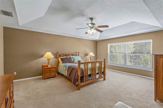 bedroom featuring a raised ceiling, ceiling fan, light carpet, and a textured ceiling