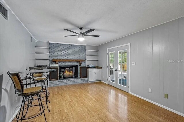 living room with french doors, crown molding, light hardwood / wood-style flooring, ceiling fan, and a fireplace