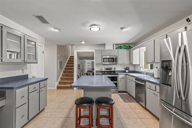 kitchen featuring light tile patterned floors, sink, appliances with stainless steel finishes, gray cabinetry, and a kitchen island