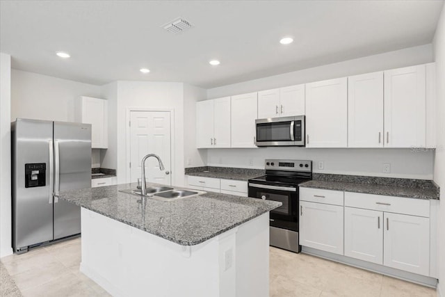 kitchen with an island with sink, white cabinets, dark stone countertops, sink, and appliances with stainless steel finishes