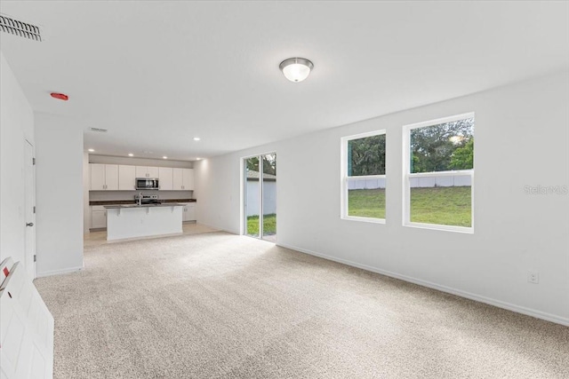 unfurnished living room featuring light carpet and a healthy amount of sunlight