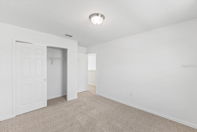 unfurnished bedroom with light colored carpet and a closet