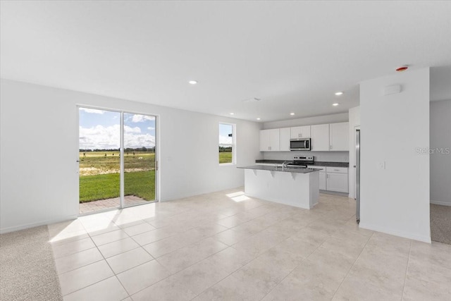 kitchen featuring a wealth of natural light, stainless steel appliances, white cabinetry, and a kitchen island with sink