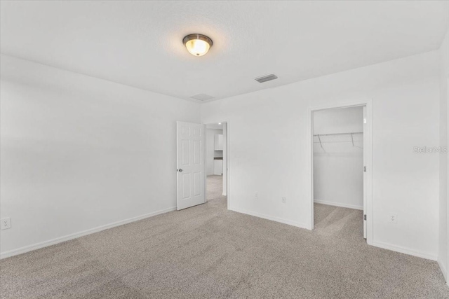 unfurnished bedroom featuring a walk in closet, baseboards, visible vents, and carpet