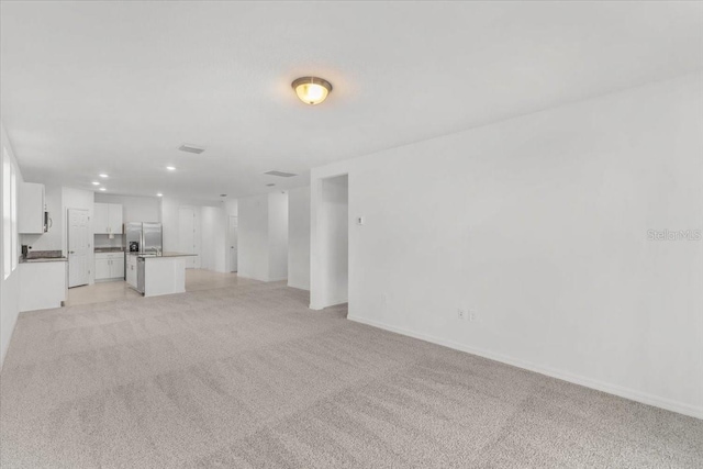 unfurnished living room featuring baseboards, recessed lighting, and light colored carpet
